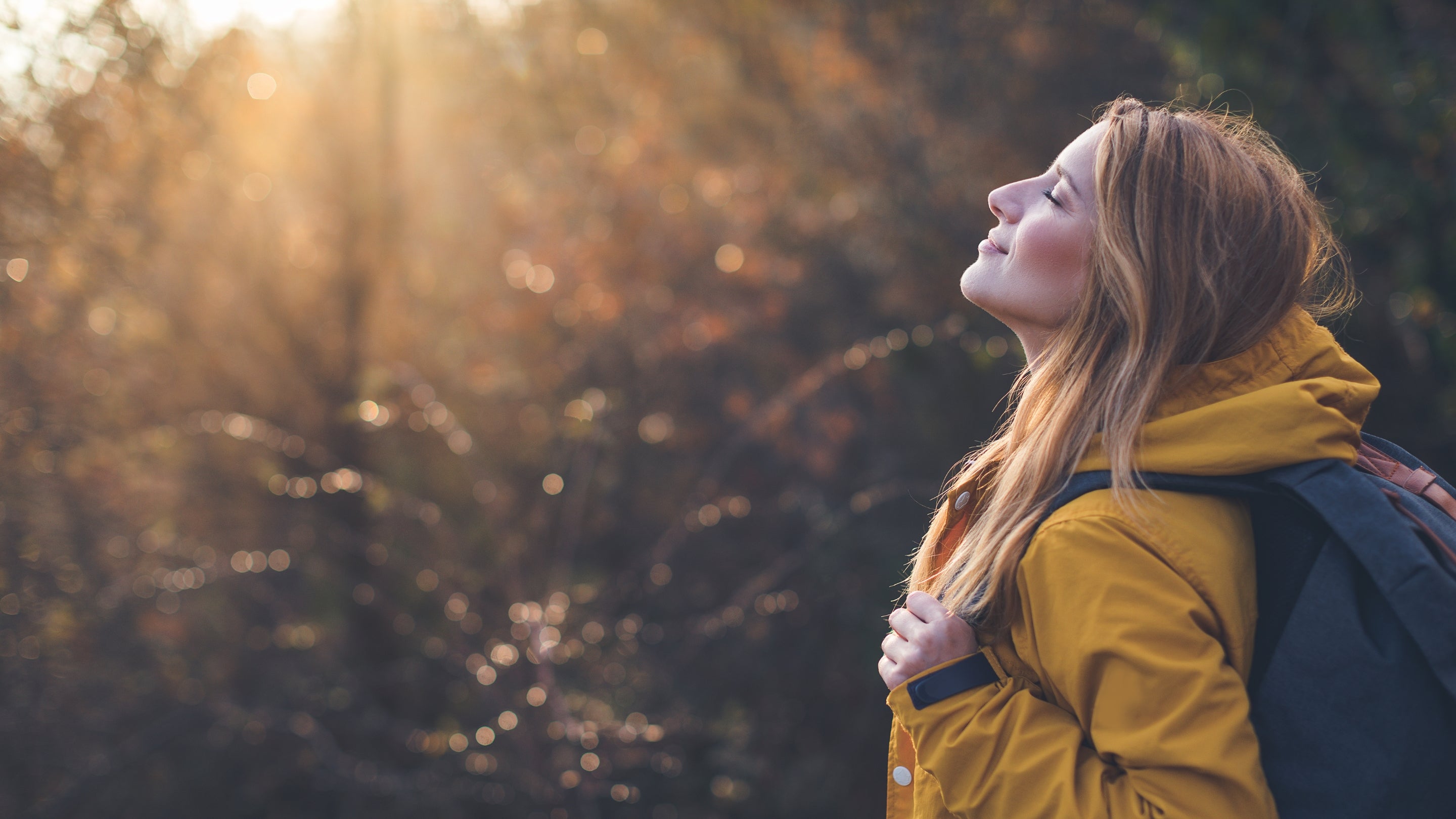 Woman in a yellow coat standing outdoors with trees in the background
