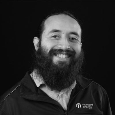 Man with a beard wearing a black jacket with 'moment energy' logo on a black background