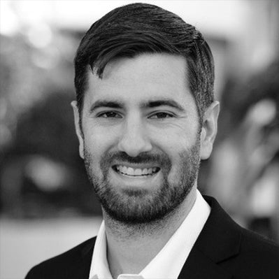 Black and white photo of a man with a beard and short hair, wearing a suit.