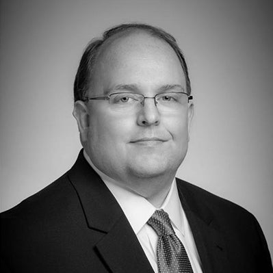 Black and white portrait of a man wearing glasses and a suit.